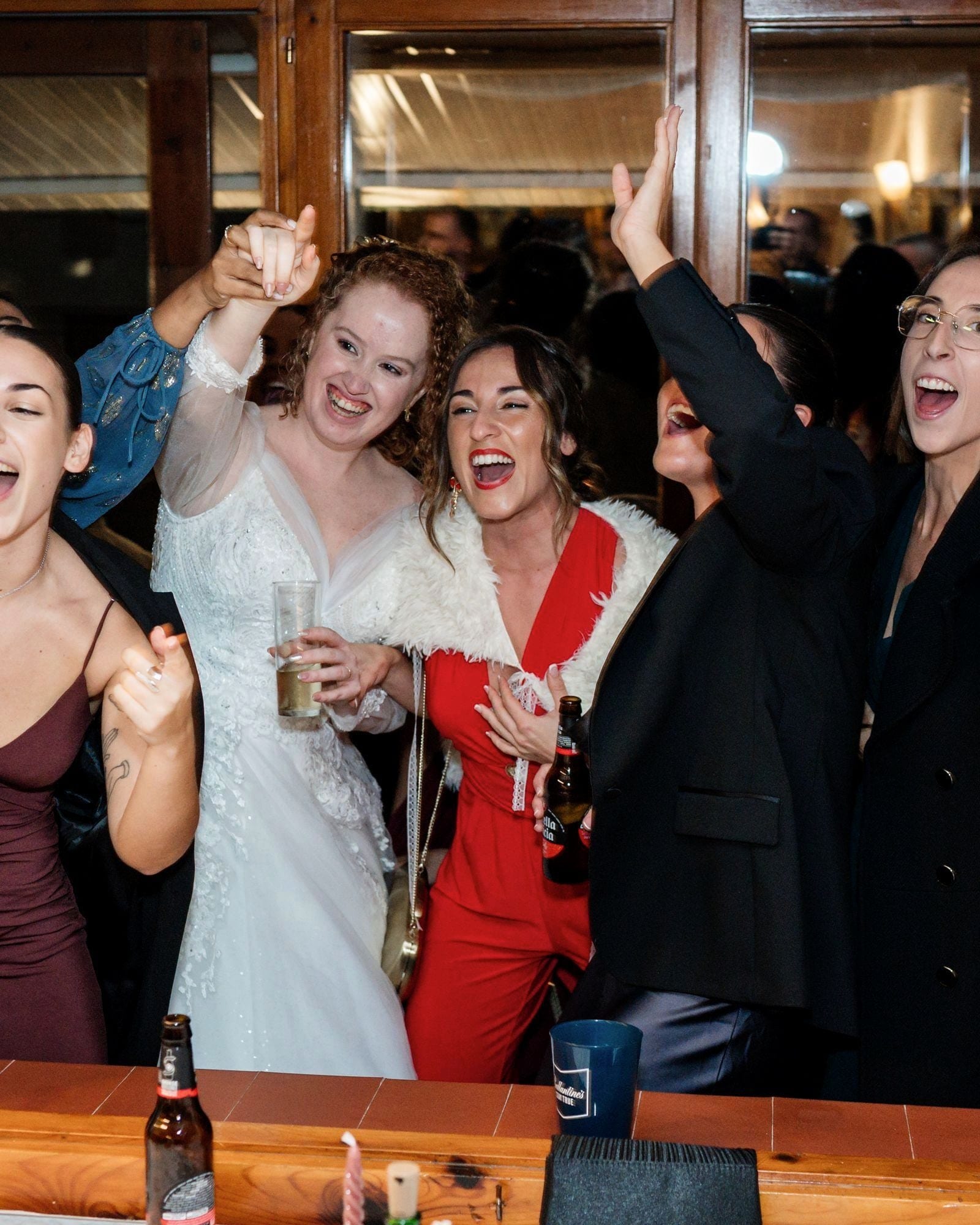 La novia y sus amigas riendo y brindando asomadas a una ventana